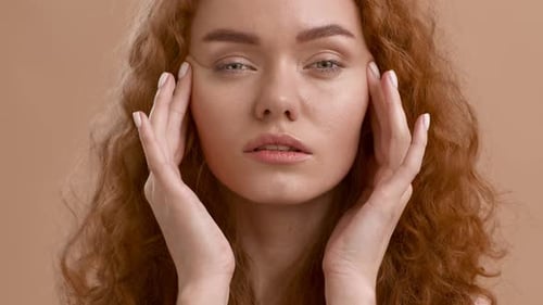 Pretty RedHaired Woman Massaging Face Posing Over Beige Background