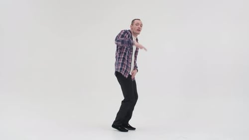 Un homme adulte à la peau claire danse des mouvements chaotiques de break dance, mettant sa jambe sur le côté et agitant