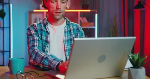 Un mec barbu travaille sur un ordinateur portable sur son lieu de travail au bureau à domicile le soir