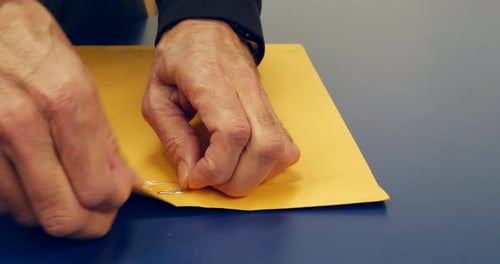 Close up on hands opening an orange envelope with important document inside after being mailed and d