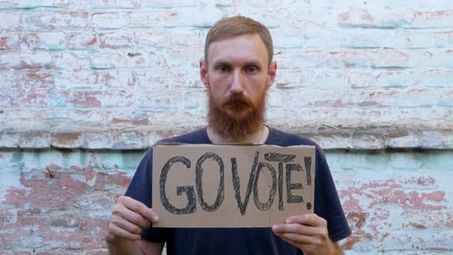 Man shows cardboard with Go Vote sign on brick wall urban background Voting concept Use your voice