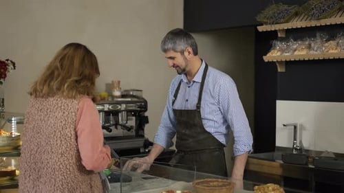 Handsome Male Cashier in Apron and Gloves Accepts Terminal Payment From Female Customer
