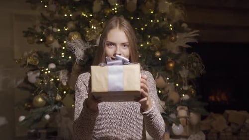 Smiling Woman Offering Christmas Gift by Christmas Tree