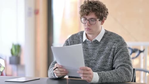 Young Man Carefully Reviewing Documents at Office Desk