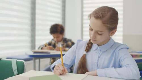 Girl and Boy Sitting at Desks and Writing