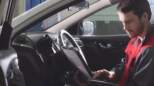 Young Technician Man Making Engine Service of Car in Garage.