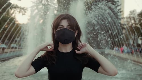 Woman Puts on Mask in Front of Fountain