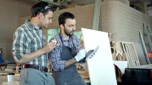 Two Carpenters Discussing Ideas One of Them Eating and Another Is Writing in Notebook at Workshop