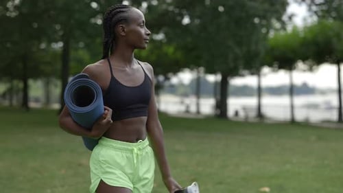 Woman Walking at Park with Yoga Mat and Bottle of Water