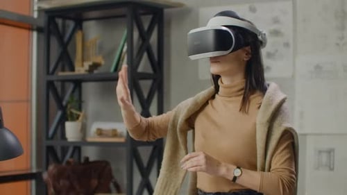 Young Woman Designer in Office in Virtual Reality Helmet with Hands Makes Movements Imitating the