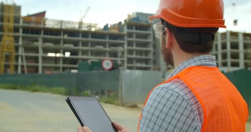 Close-up Portrait of Engineer with Gadget on Background of Building Under Construction. Modern
