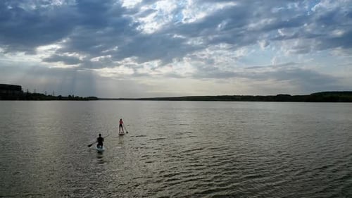 Young Adults Paddleboarding on Lake Under Cloudy Sky