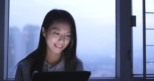 Woman Uses Tablet Indoors Near Window at Night