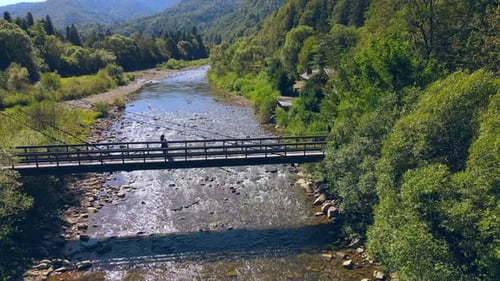 Aerial View From Old Wooden Suspension Bridge Over a Mountain River. Girl Standing on a Wooden