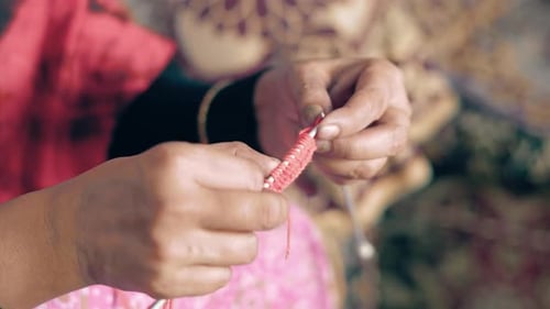 Woman's hands doing the knit work tie-up hand work. Close up of process of knitting with red wool