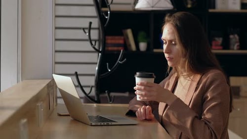 Young woman sitting by the window at the bar counter in coffee shop.