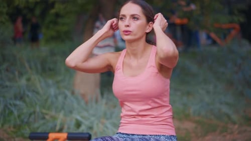 Femme athlétique faisant des exercices d'abdos sur un banc, une machine d'exercice, une salle de sport extérieure dans un parc