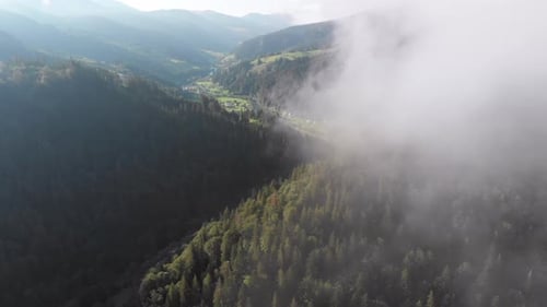 Volando entre las nubes sobre el valle montañoso de los Cárpatos con un pueblo en verano