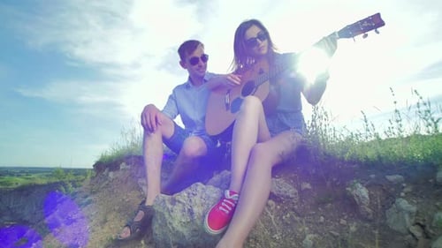 Junges Paar sitzt und spielt Gitarre