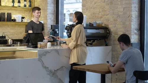 Wide Shot of Young Beautiful Woman Paying for Coffee Using Smartphone and Leaving with Cup
