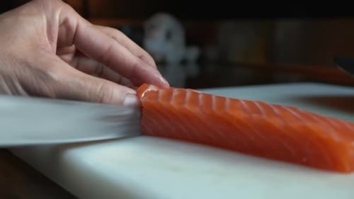 Close Up View of a Hand with a Knife Cutting Salmon Into Thin Slices