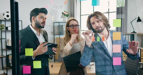Team Standing Near Glass Wall in Modern Office and Brainstorming New Ideas Using Sticky Notes