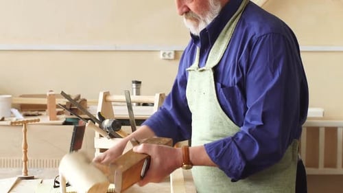 Senior Man Using Plane on Wood in Workshop