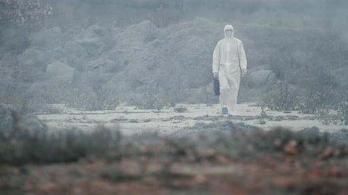 Labortechniker in Maske und chemischem Schutzanzug geht auf trockenem Boden durch giftigen Rauch.