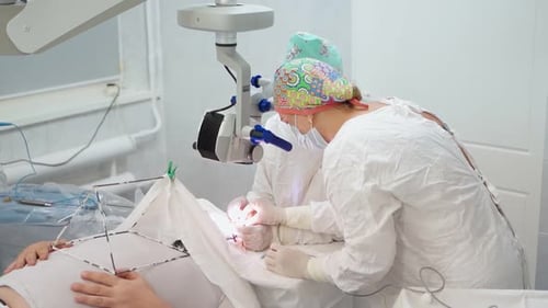Two Female Surgeons Perform Eye Surgery with Microscope and Medical Instruments