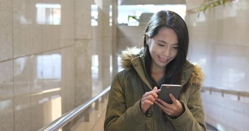 Young Woman Uses Smartphone Indoors in Urban Setting