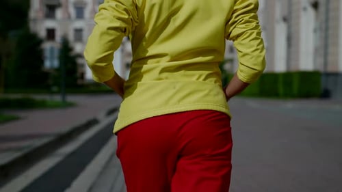 a Female Body in a Yellow Jacket and Red Pants is Walking Near City Buildings