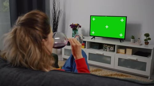 Woman Sits on Couch Drinking Wine and Watches TV