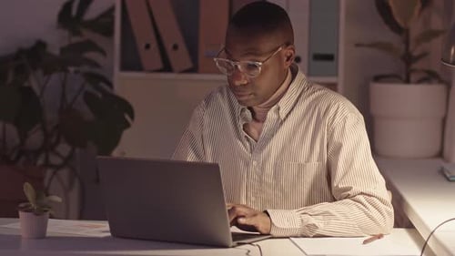 African-American Man Working on Laptop in Office at Night