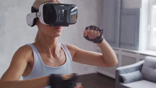 Young and sporty girl in sportswear is doing exercises at home using virtual reality helmet.