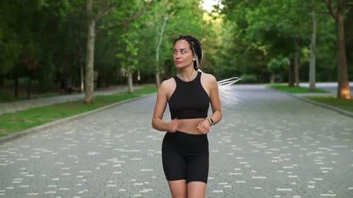 Front View of European Woman with Black and White Dreadlocks Running By Local Green Park in the City