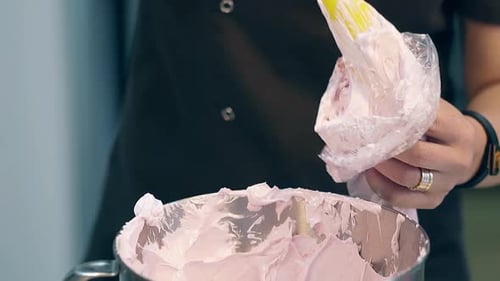 Un pâtissier met de la crème dans une poche à douille pour décorer le gâteau