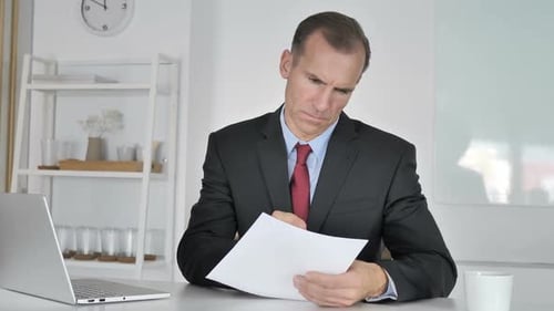 Geschäftsmann mittleren Alters liest Dokumente im Büro