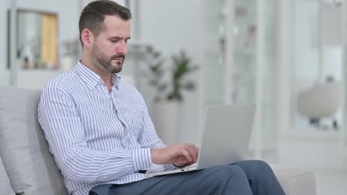 Man Typing on Laptop Massages Temples Indoors