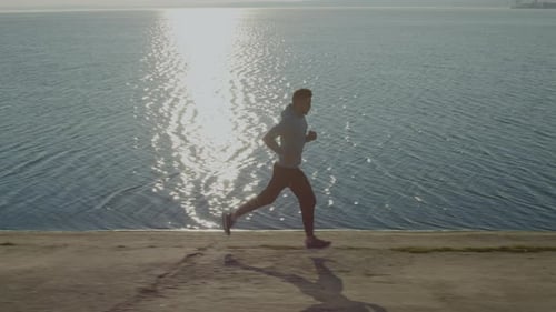 Athletic Man Jogging Along Water at Sunrise