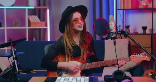 Fille au chapeau et aux lunettes interprétant une nouvelle chanson devant un équipement d'enregistrement aux sons de la guitare