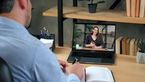 Mann, Student, studiert online per Videokonferenz, Laptop, schreibt in Notizbuch