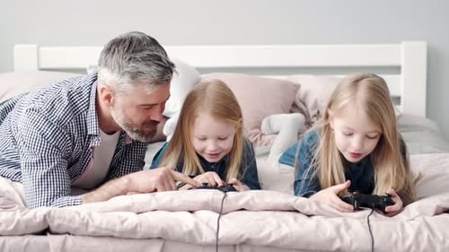 Father and Daughters Play Video Games on Bed