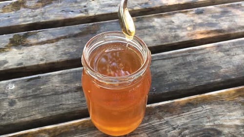 Golden Honey Drips from Spoon into Jar
