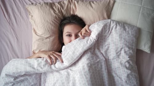 Top View of a Young Attractive Woman Stretching Hands While Lying in Bed in the Morning