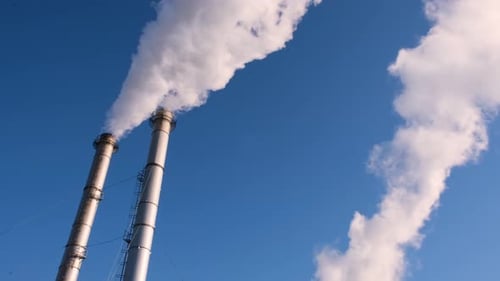 Industrial Smokestacks Releasing White Smoke Against Blue Sky