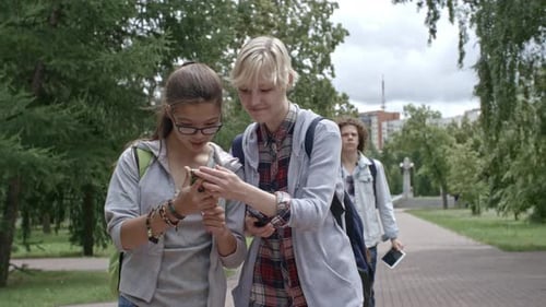 Teen Girls Using Smartphones while Walking in Park