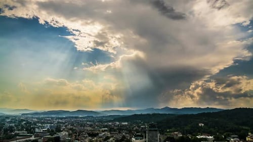 Sonnenstrahlen durchdringen Wolken am himmlischen Himmel über Mountain Resort City, Zeitraffer