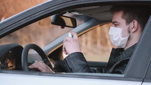 Man Wearing Mask Sprays Hand Sanitizer in Car