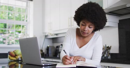 Woman Writing in a Notebook in Kitchen