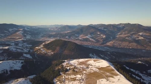 Aerial View of Small Village with Scattered Houses on Snow Covered Hills in Winter and Bare Dark